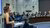 Vrouw praat door de microfoon met verschillende professoren op de achtergrond.