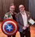 Two men with glasses and superhero props smiling into camera