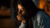 Person in gray hoodie leaning on hand in dimly lit, warm-toned room.