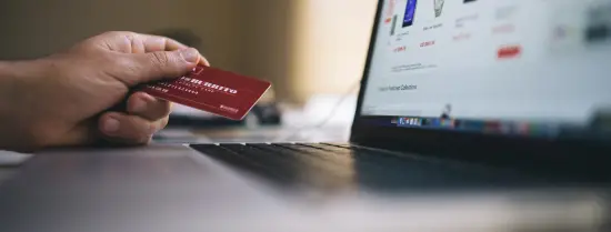 Person holding a creditcard in front of a laptop at a webshop.