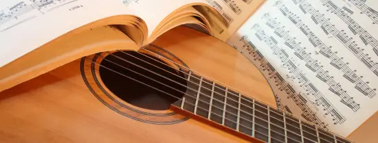 Guitar with a book of music notes covering part of the guitar